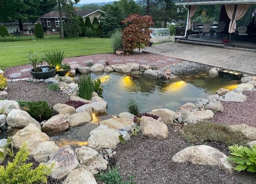 The same backyard transformed into a lit pond and stream at dusk