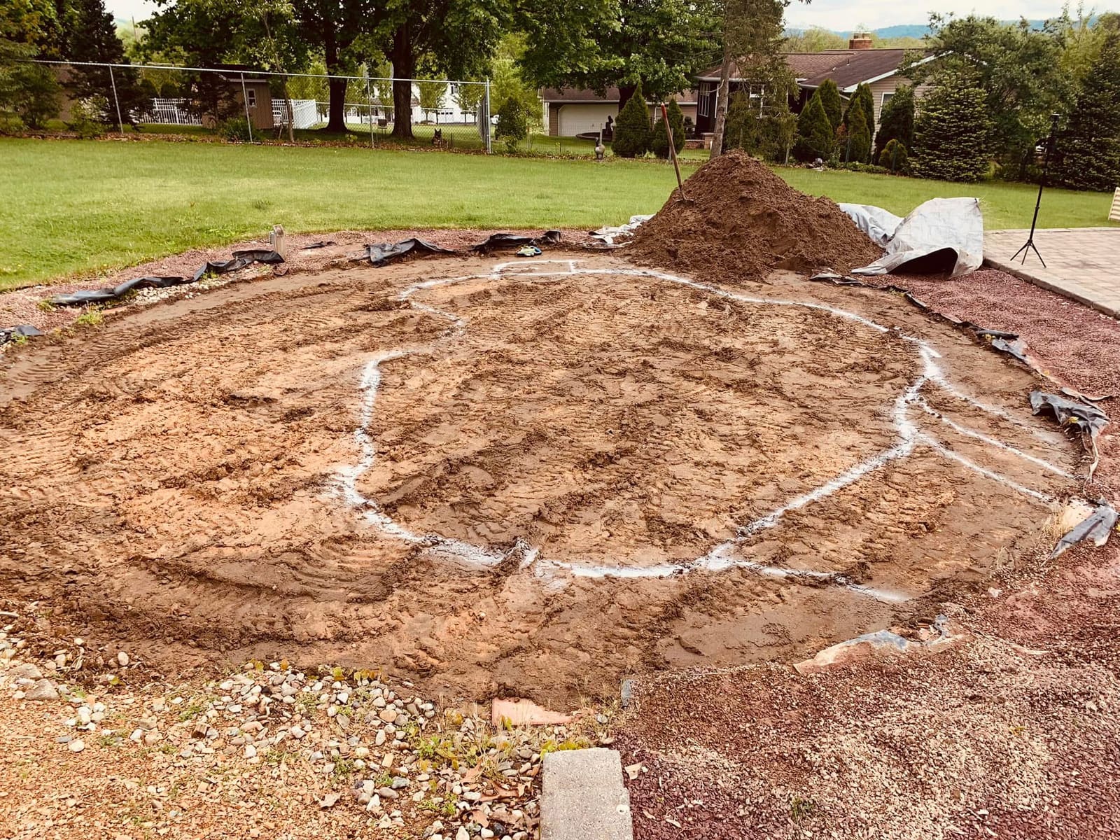 Chalk-outlined pond excavation area beside a paver patio before construction